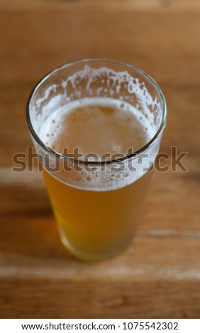 Pint of India Pale Ale beer on blond wood table, with head dissolved, emphasizing lacing on glass