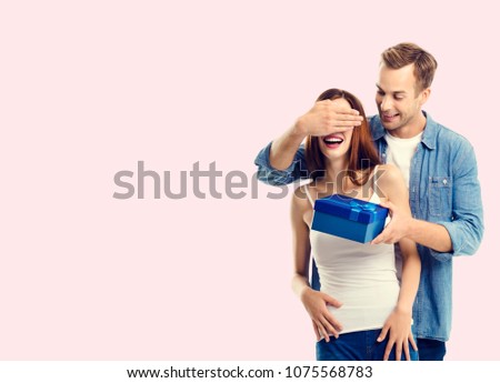 Happy couple with gift box, close to each other, with copyspace empty area for slogan or advertising text message, over pink background. Love, holiday, sales, shop concept studio shot.
