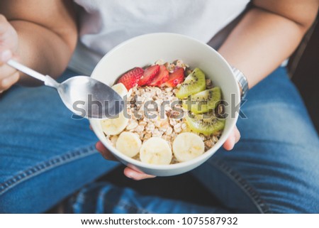 Eating healthy breakfast concept. Woman holding bowl of cereal and granola and variety fruits and glass of milk on th floor in the morning at home. Royalty-Free Stock Photo #1075587932