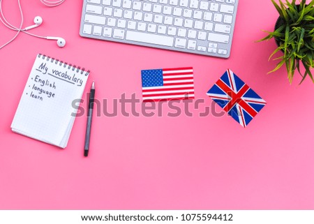 Learn new english vocabulary. Learn landuage concept. Computer keyboard, british and american flags, notebook for writing new vocabulary on pink background top view copy space