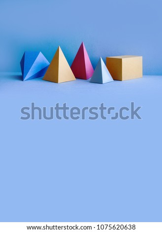 Colorful abstract geometrical composition. Three-dimensional prism pyramid rectangular cube objects on blue background. Yellow blue red green colored solid figures, vertical copy space photo