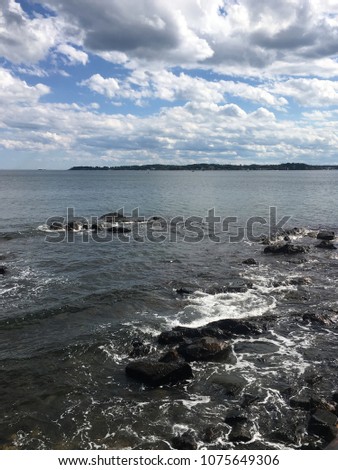 Beverly, Massachusetts / United States - September 8, 2017: Storm clouds clearing to blue sky as waves wash over rocks in the harbor
