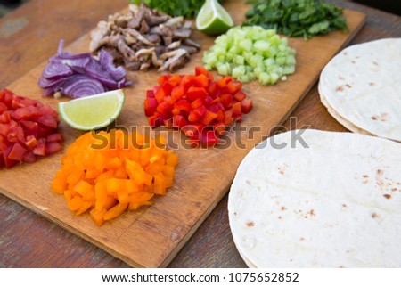 Tacos ingredients. Set of chopped fresh vegetables with beef, lime and tortillas on wooden board. Side view.