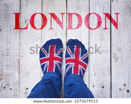 Selfie feet wearing socks with British flag pattern on white wooden grunge floor background with red London text. 