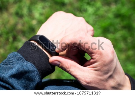 Fitness bracelet or smart watch on a man's hand. Against the background of green grass. An adult male in a blue band. Healthy lifestyle concept