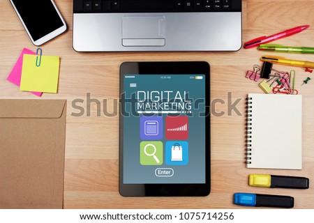 Digital tablet with DIGITAL MARKETING on blue screen with office supplies on wooden desk