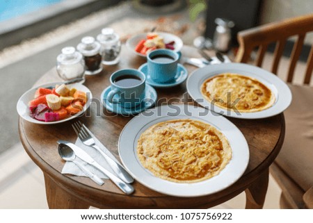 Plates with banana pancakes, tropical fruits and two cups of coffee on wooden table