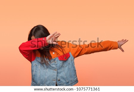 Anonymous girl in colorful denim jacket standing in dab dance pose on orange background.  Royalty-Free Stock Photo #1075771361