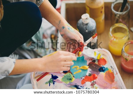 Close up of girl`s hands holding paint brush and mixing colors for painting.