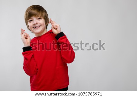 Cute confident little caucasian boy in red sweater showing hope gesture on grey background