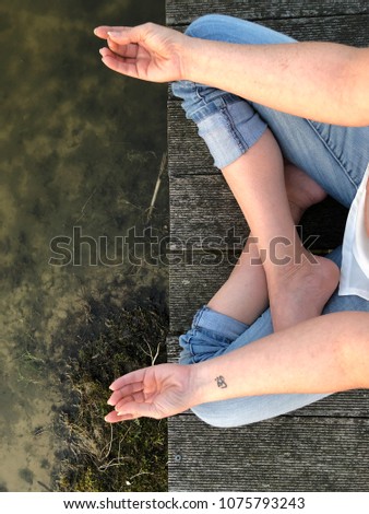 Young woman practices yoga and meditates in the lotus position on the peer of a lake on a sunny evening