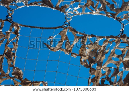 White military mesh with torn holes with shadows from bright sunlight. Camouflage net and the blue sky.