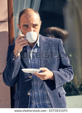 Picture of handsome man walking on the street and looking aside while holding cup of coffee.