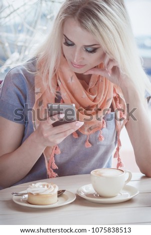 Beautiful woman in the cafe with a cup of cappuccino and a phone in the hand, soft focus background