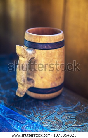 Very soft focus. Vintage looking picture. Wooden beer mug on the wooden table curved with ancient, viking patterns. Close-up at rustic wooden beer mug.