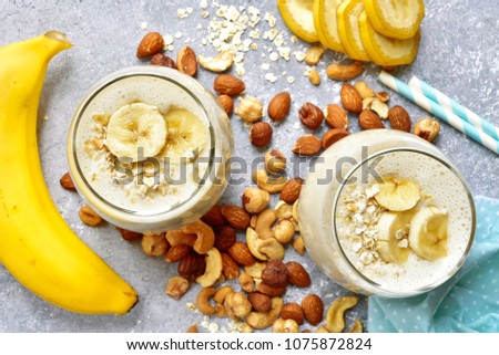 Homemade banana nut smoothies with ingredients for making over light grey slate, stone or concrete background.Top view.