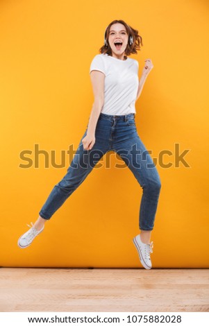 Image of emotional funny young woman jumping isolated over yellow background listening music.