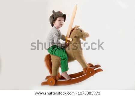 Funny child in old military cap with red star, on toy horse-rocking horse with wooden sword. Boy dreams of battles, victories and adventures. Concept training of spirit, education morale, patriotizm 