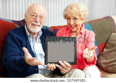 Senior couple holding up a blank tablet PC, ready for your text or picture.