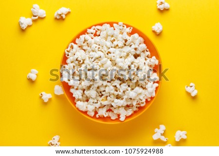 Popcorn in an orange bowl on yellow background. Horizontal image. Top view. Royalty-Free Stock Photo #1075924988