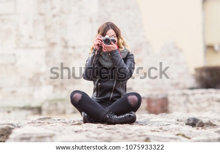 Hipster photographer girl in leather coat sitting with vintage DSLR camera