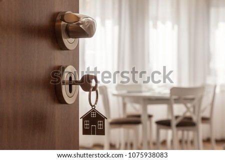 Open door to a new home. Door handle with key and home shaped keychain. Mortgage, investment, real estate, property and new home concept Royalty-Free Stock Photo #1075938083