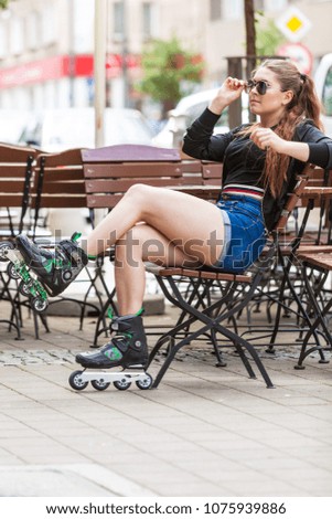 Happy joyful young woman wearing roller skates sitting in town. Female being sporty having fun during summer time.