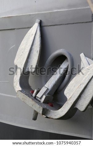 Close up outdoor view of two heavy anchors hanging at a front of a boat. Detail of a grey and black painted wooden ship. Abstract image of maritime objects. Bright surface. Simple picture in a port.  