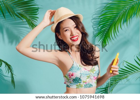 Pretty smiling asian woman enjoys good music in earphones standing over blue background