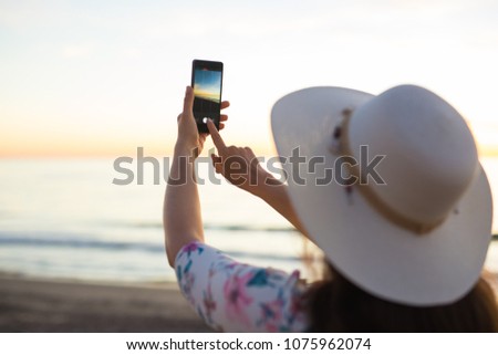 Young woman taking photo the sea and sunset with cell phone or smartphone digital camera for Post to Online Internet While travel on vacation holiday.