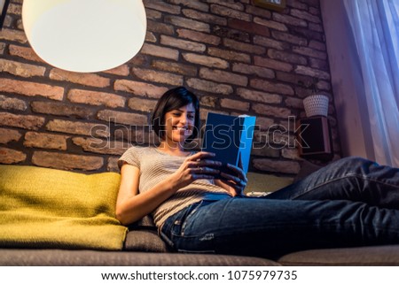 Beautiful woman home at night reading book  Royalty-Free Stock Photo #1075979735