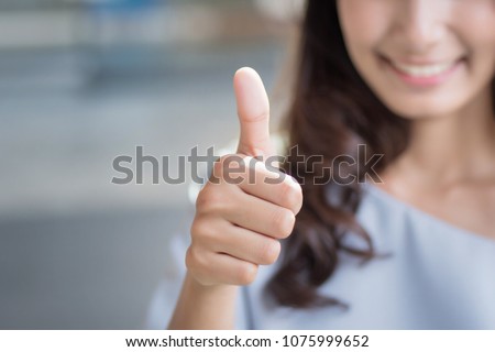 successful girl pointing thumb up; portrait of cheerful smiling woman pointing up approving, yes, ok, good, thumb up gesture; asian woman young adult model Royalty-Free Stock Photo #1075999652