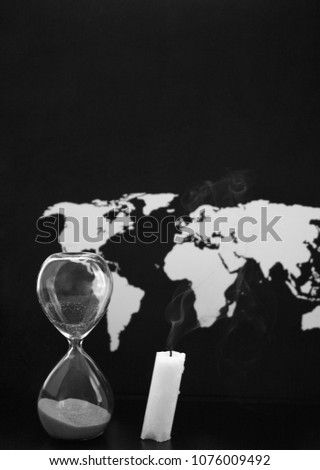 Monochrome image, world map, sandglass and burnt candle, black background