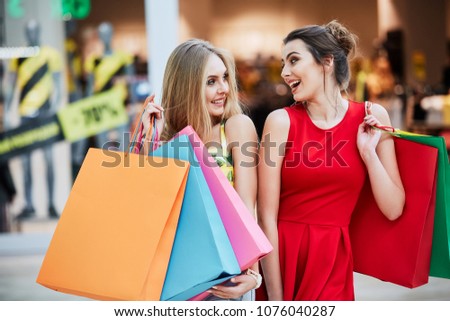 Lovely girls standing with colorful bags at shopping mall background during shopping process and smiling, shopping concept, shopping center.