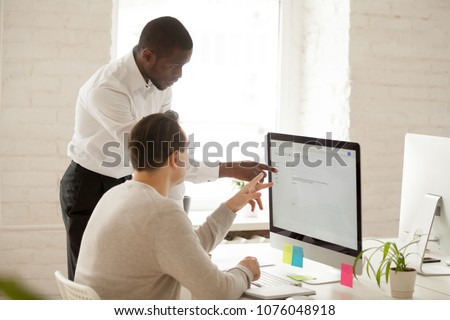 African team leader helping colleague with computer work explaining coworker new corporate application usage, black mentor teaching intern supervising and giving instructions about emails in office Royalty-Free Stock Photo #1076048918