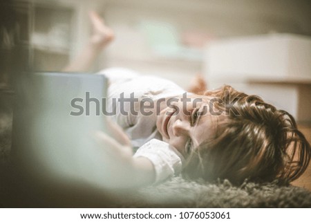 Smiling little girl lying on floor and using digital tablet.