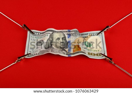 Close up one hundred US dollar paper currency banknote pulled and stretched over red background with copy space, high angle view