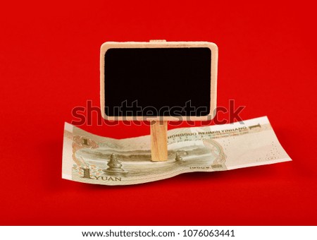 Close up one Chinese Yuan paper currency banknote and blank chalk blackboard sign with copy space over red background, high angle view