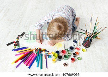 Child drawing picture with crayon  in album using a lot of painting tools. Creativity concept.