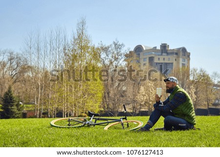 Young man on the lawn with a bicycle. He holds a glass of coffee in his hand. Leisure in the city