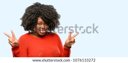 Beautiful african woman looking at camera showing tong and making victory sign with fingers, blue background