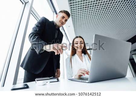 a young, handsome businessman in a suit to show his beautiful girl  helpers how to work on a laptop, they smile in a pretty style office