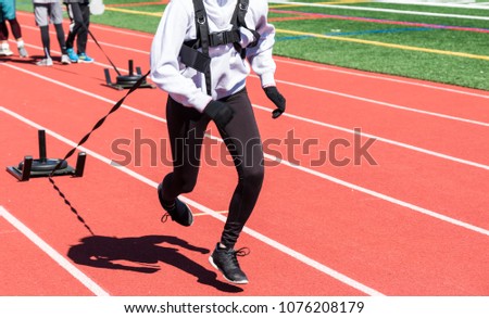 Runners, sprinters on a boys and girls high school track and field team run while pulling a sled with weights on it, on a track.