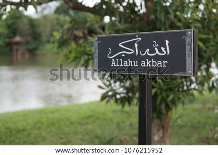 An Arabic verse signpost with background of a park. Allahu akbar is an Arabic verse in Islamic practice that means "Allah is the greatest".