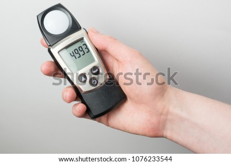 man holds in his hand an instrument for measuring illumination