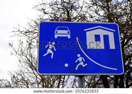 Blue road sign courtyard territory children playing football on trees and sky background.
