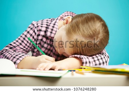 Isolated shot of child with poor posture sitting at desk and do homework. Girl rested her head on table and writes in notebook. Royalty-Free Stock Photo #1076248280