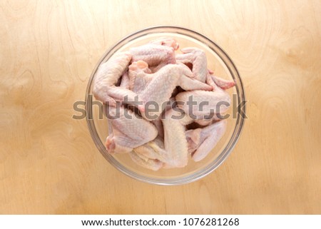 Chicken wings in a glass bowl. A glass dish with raw wings on a wooden table.