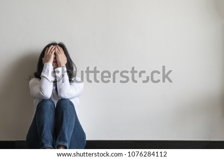 Panic attack woman, stressful depressed emotional person with anxiety disorder mental health illness, headache and migraine sitting feeling bad with back against wall on the floor in domestic home Royalty-Free Stock Photo #1076284112