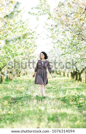 beauty, women day, freedom concept. between two lines of cherry trees in bloom young and charming woman is walking bare feet and smiling, she is wearing middle dress with flower print